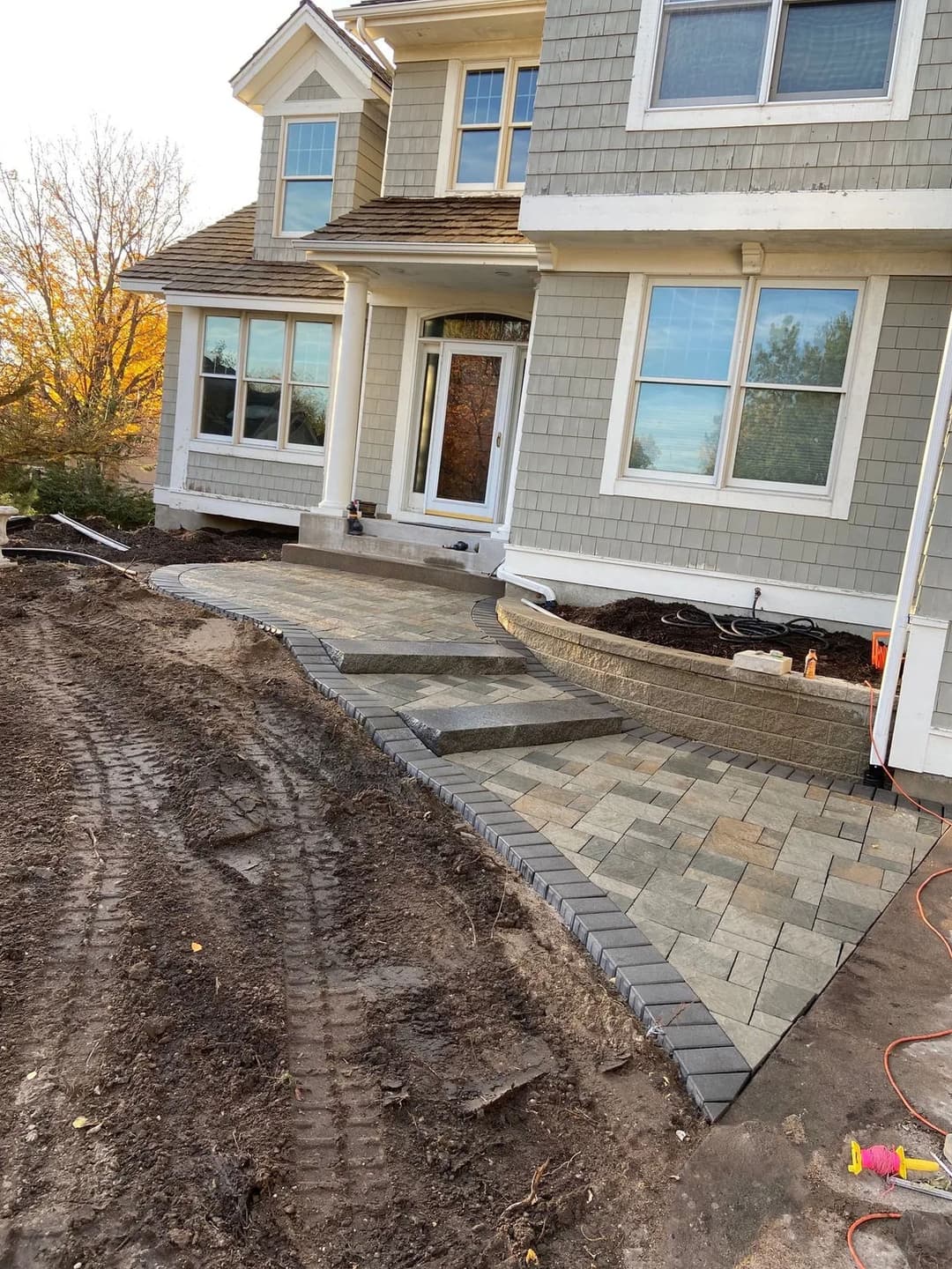 Newly installed paver walkway and patio in front of a modern home with landscaping preparation.