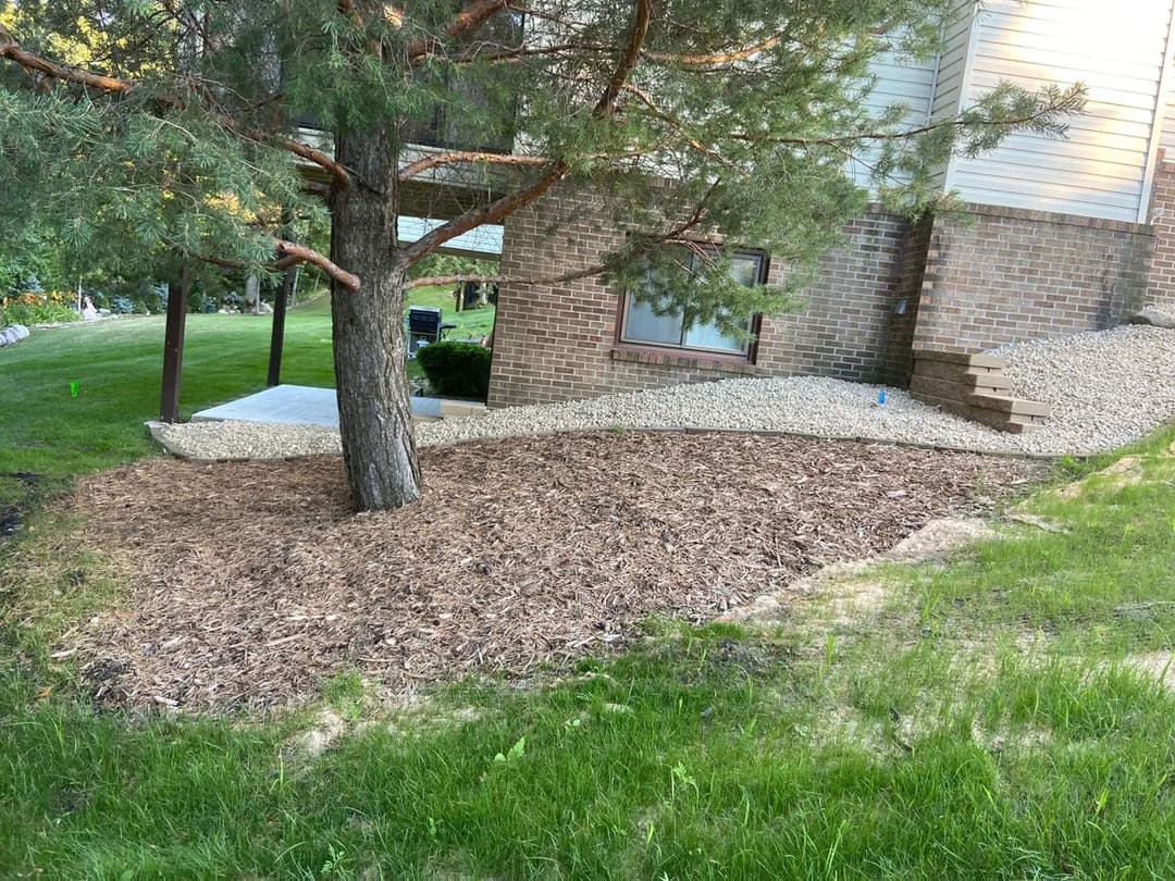 Landscaped yard with mulch, tree, and gravel pathway near a home.