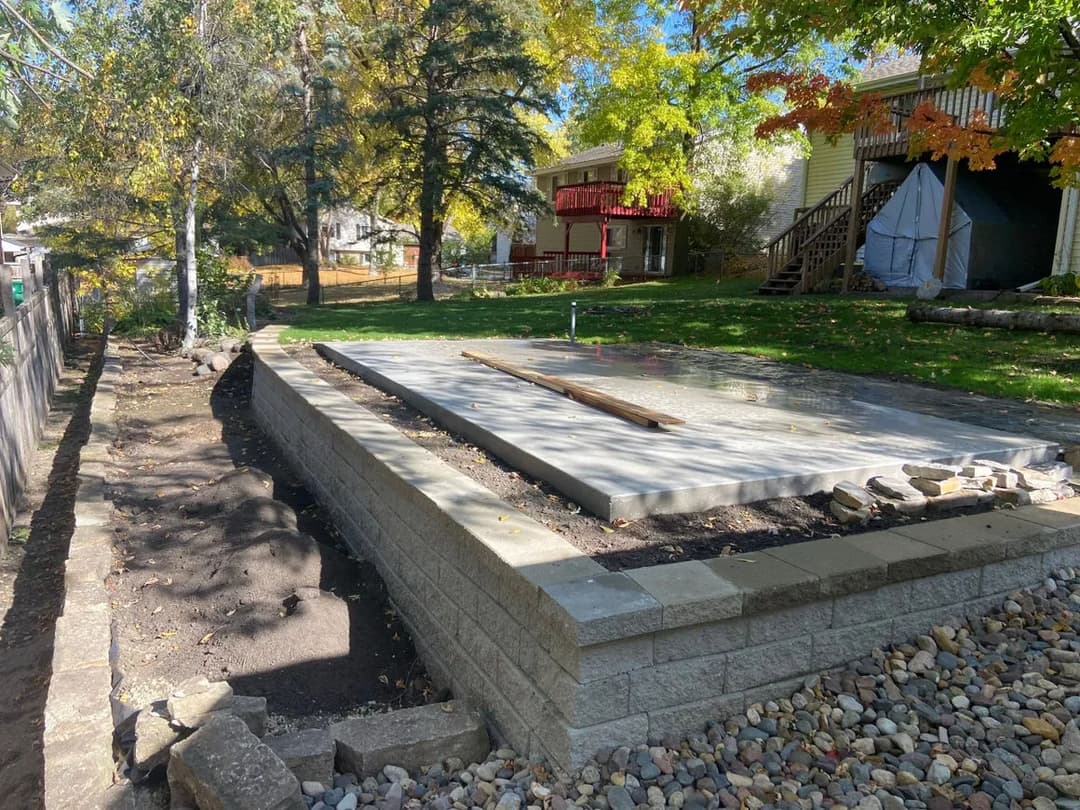 Concrete foundation slab in a residential backyard, surrounded by trees and landscaping.
