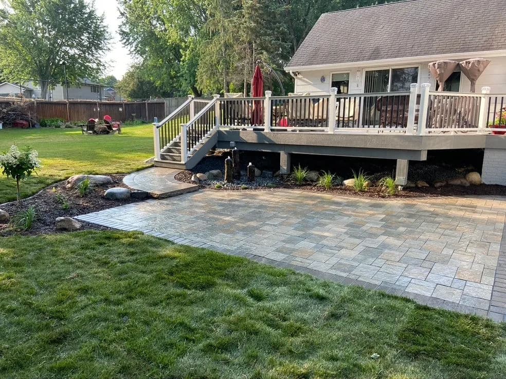 Backyard patio with stamped concrete, landscaped garden, and a deck overlooking green lawn.