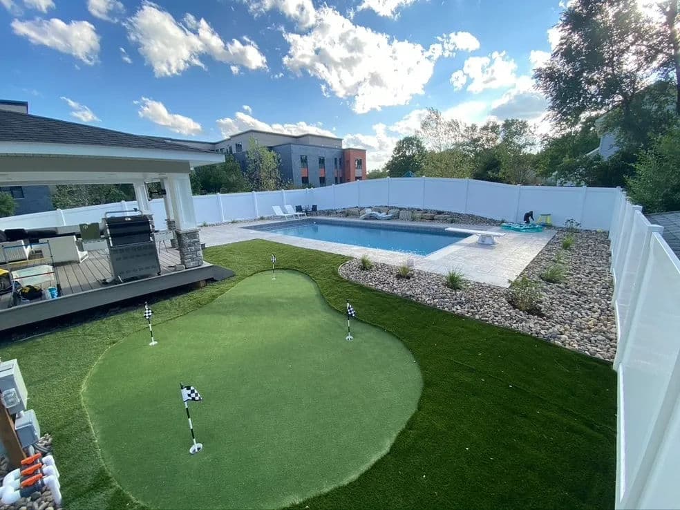 Backyard oasis with swimming pool, putting green, and modern patio furnishings under blue skies.