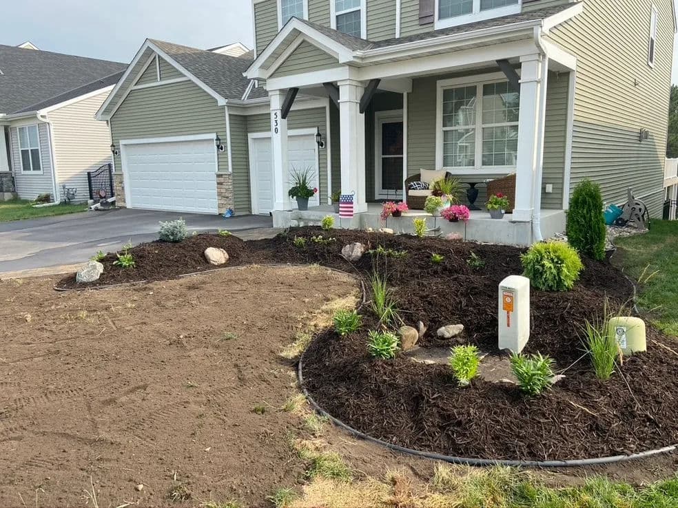 Newly landscaped front yard with mulch, plants, and decorative stones in a suburban home.