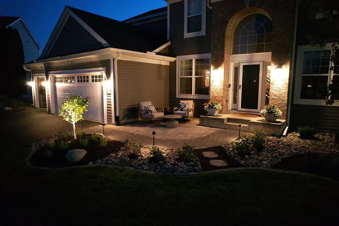 Illuminated front porch and landscaped path at night with stone details and planter boxes.