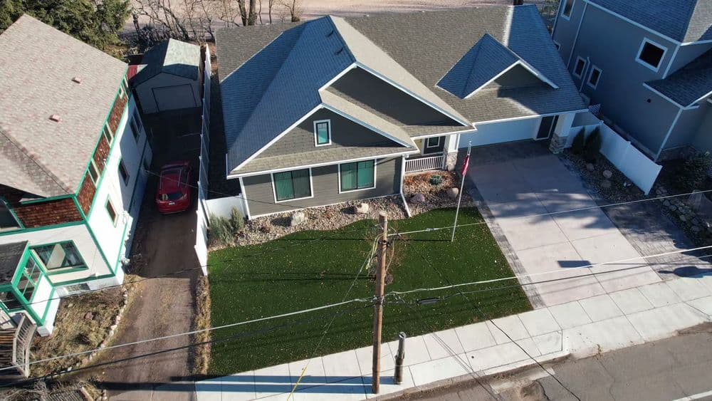 Aerial view of a modern gray house with manicured lawn and driveway in a residential area.