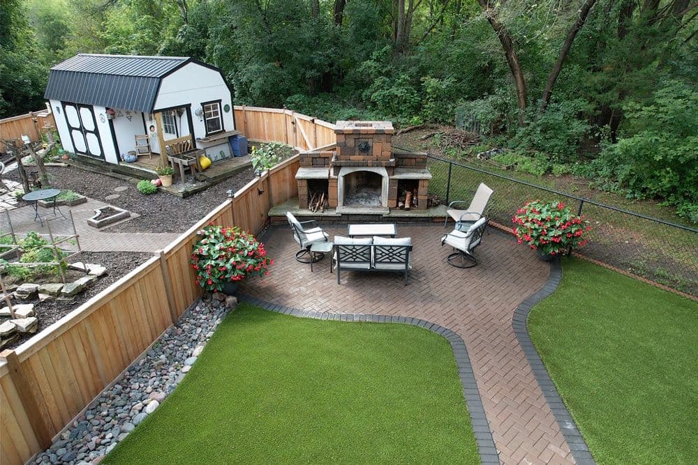 Lush backyard with a patio, garden, outdoor fireplace, and a charming shed surrounded by greenery.