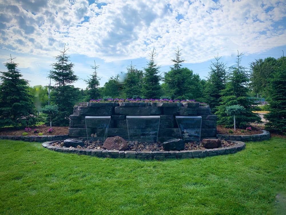 Decorative stone water feature surrounded by lush greenery and colorful flowers.
