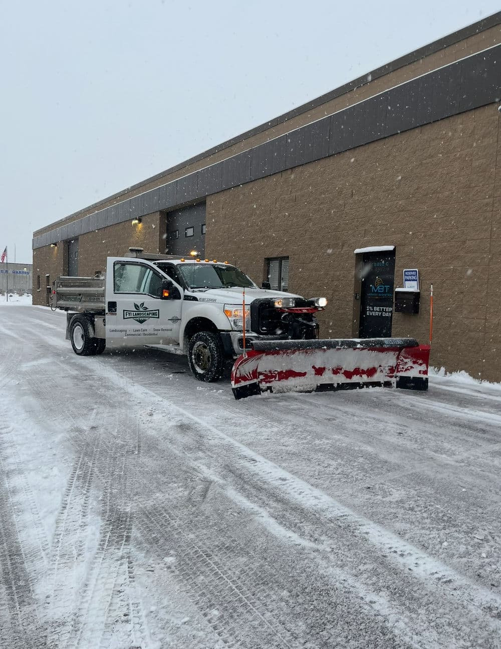 Snow plow truck clearing snow in front of a commercial building on a snowy day.