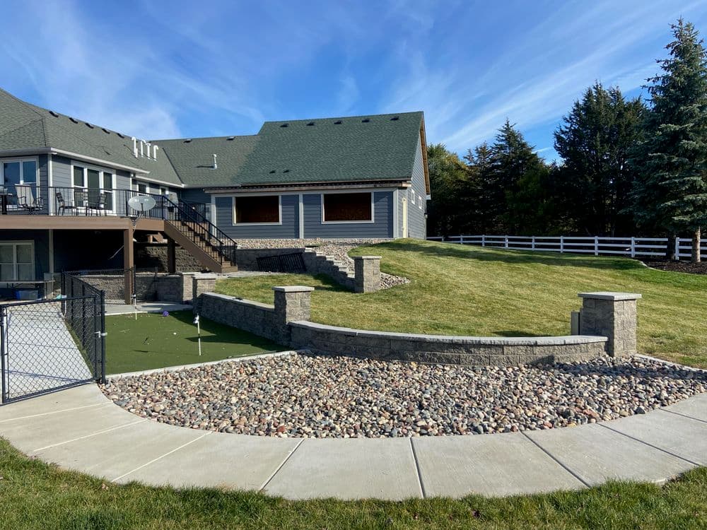 Landscape design featuring a backyard with stone features, green lawn, and a modern home.