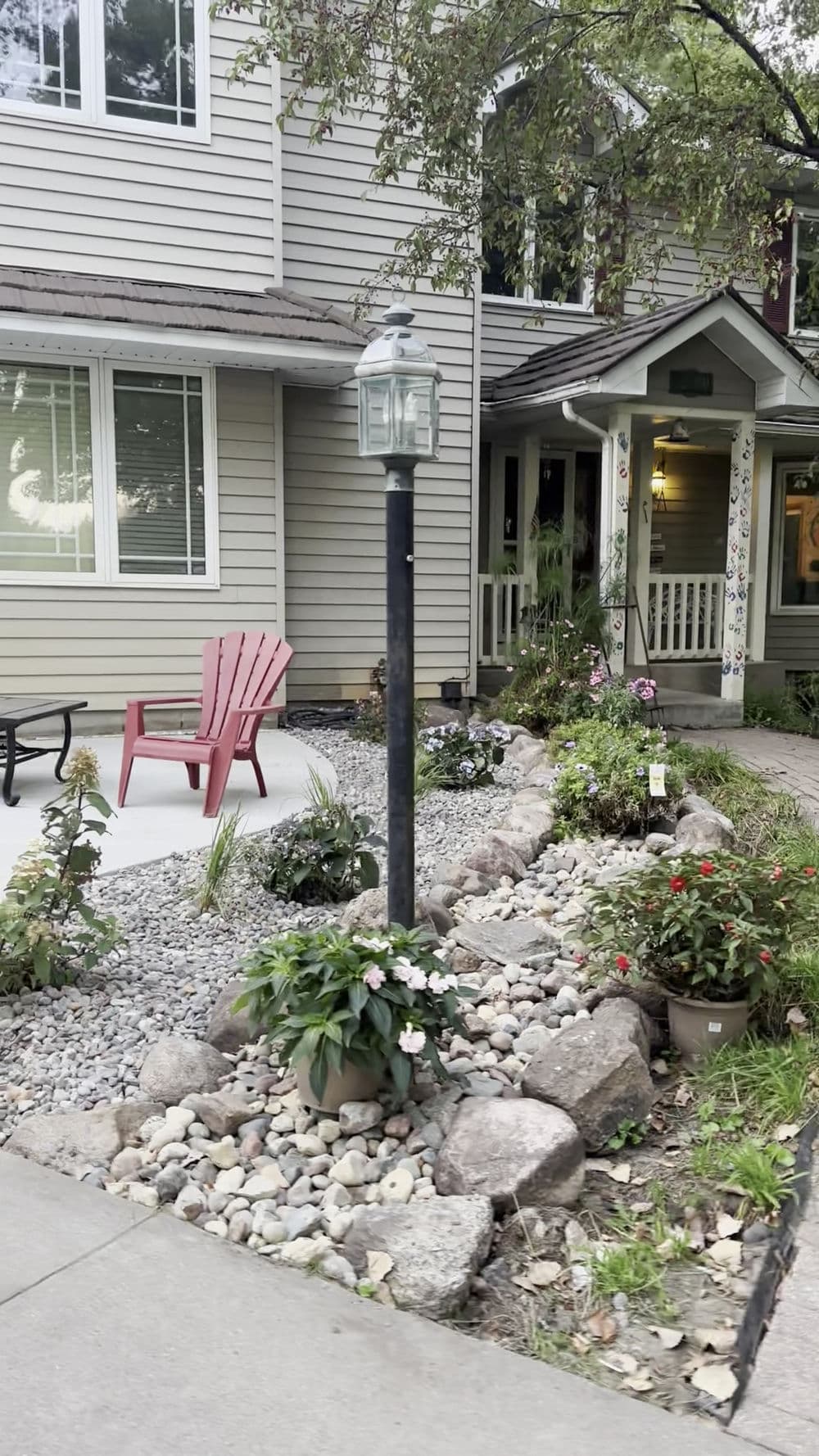 Charming front yard with landscaped stones, vibrant flowers, and a lantern beside a cozy porch.