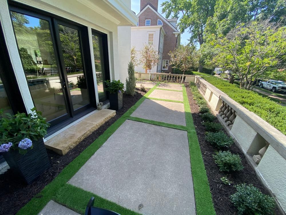 Lush home garden walkway with grass borders, potted plants, and stone path.