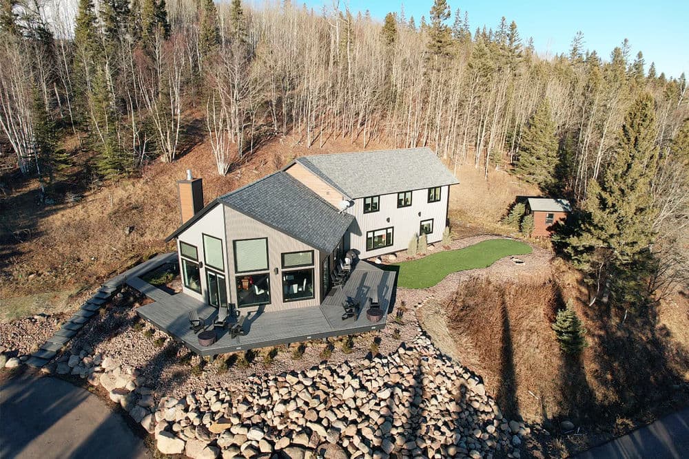 Modern home in wooded area with large deck and landscaped yard, surrounded by trees.