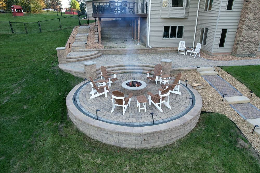 Outdoor fire pit area with circular stone seating, surrounded by a lush green lawn.