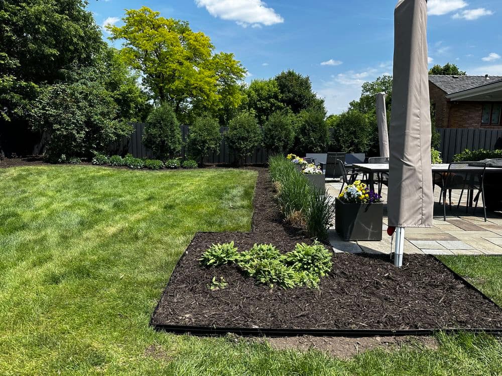 Lush green lawn with landscaped garden beds and outdoor dining area in sunny backyard.